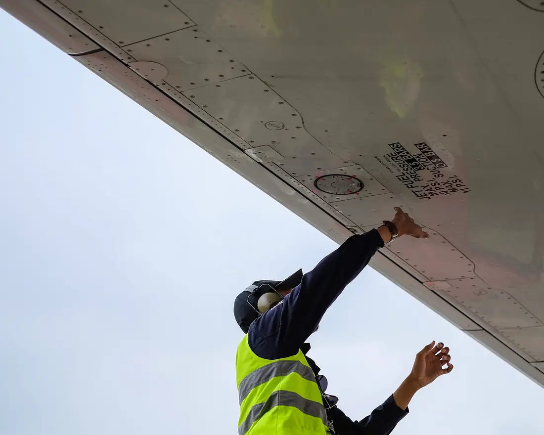 Ground crew member in a high-visibility vest inspecting an aircraft wing